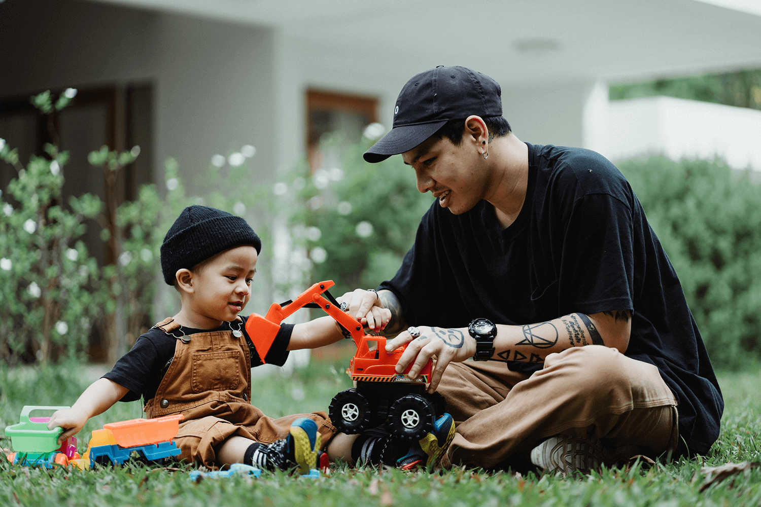 A dad and child playing with toy trucks and excavators outside.