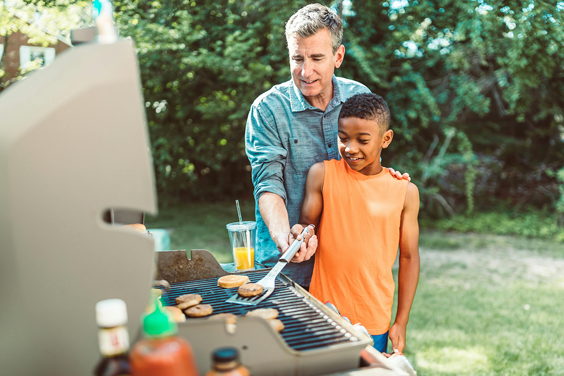 A father teaching his son how to do outdoor grilling.