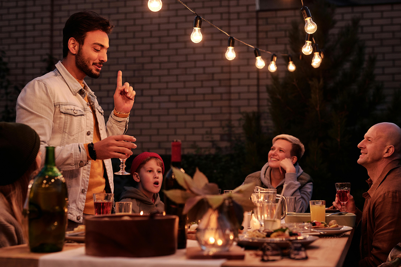 A man speaking at a table during a whodunit party.