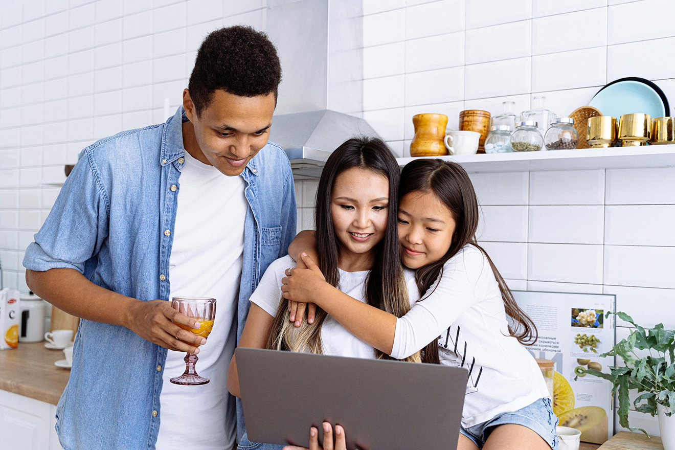 A family of three meal planning on a laptop in the kitchen.