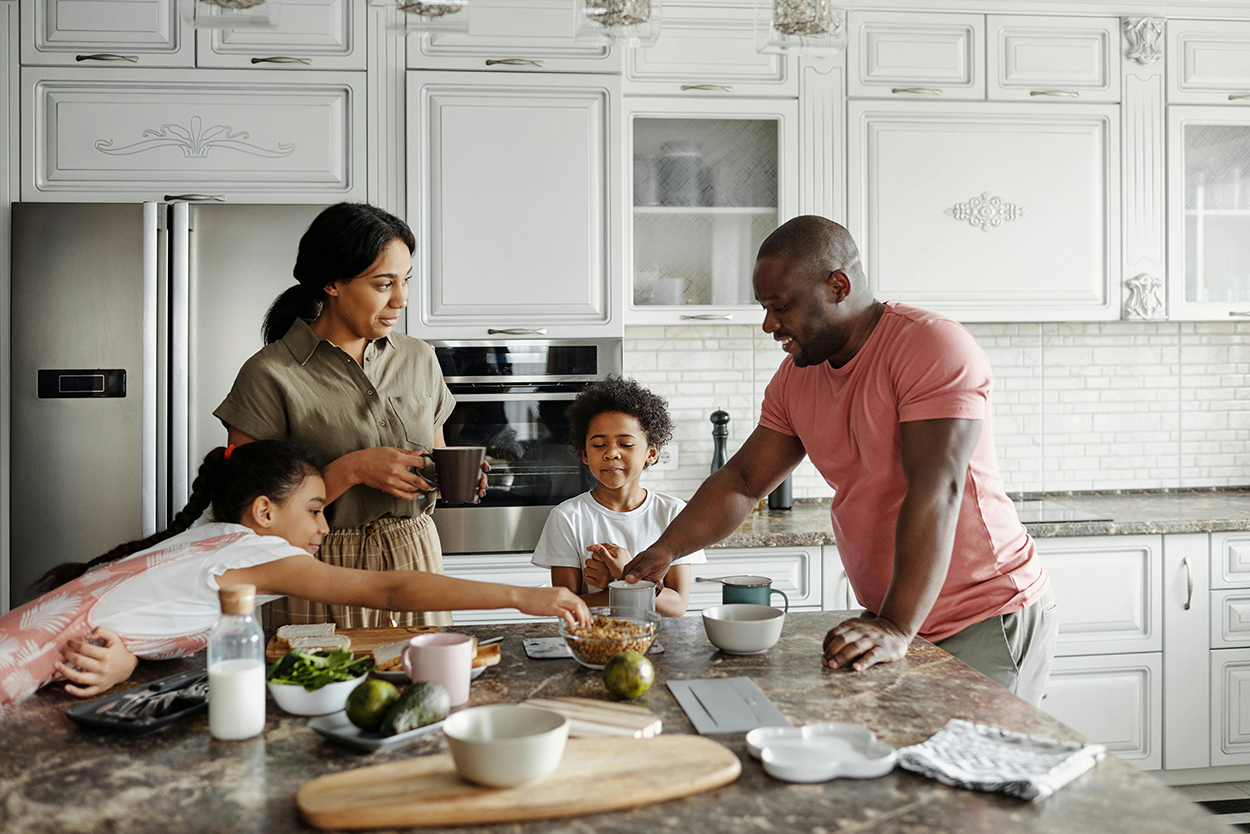 A family of four standing around a kitchen island and making time to share a meal.