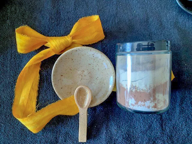 Jar of face mask powder and a stone spoon and mixing bowl.