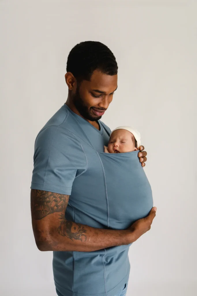 A dad holding his baby in a baby-carrying shirt.