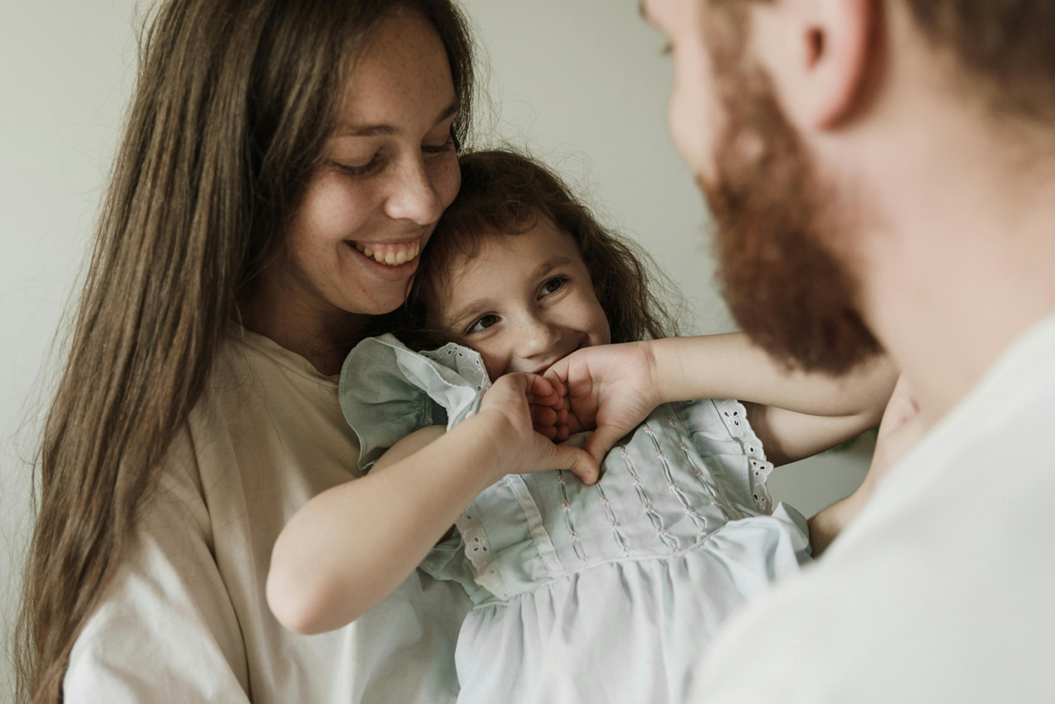 A girl making a heart shape with her hands and showing her parents.