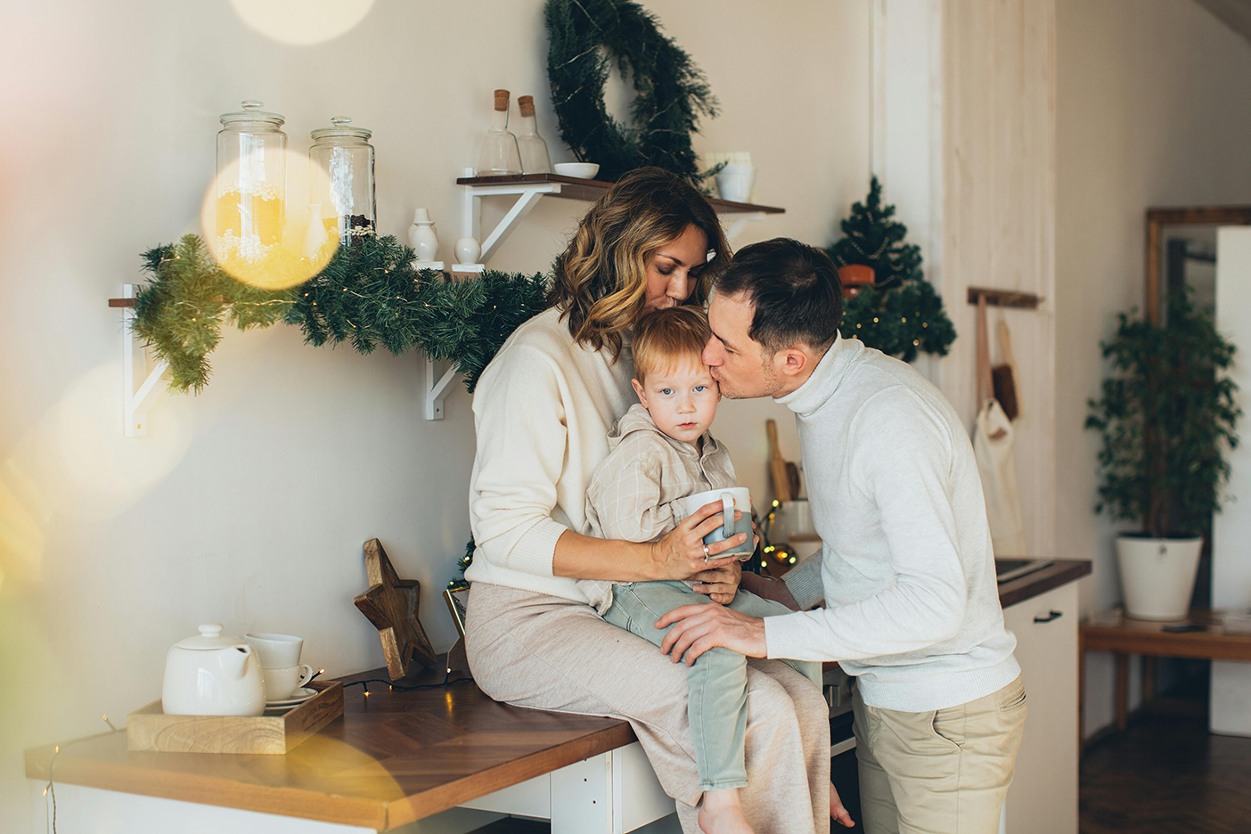 Parents kissing their foster care child in the kitchen.