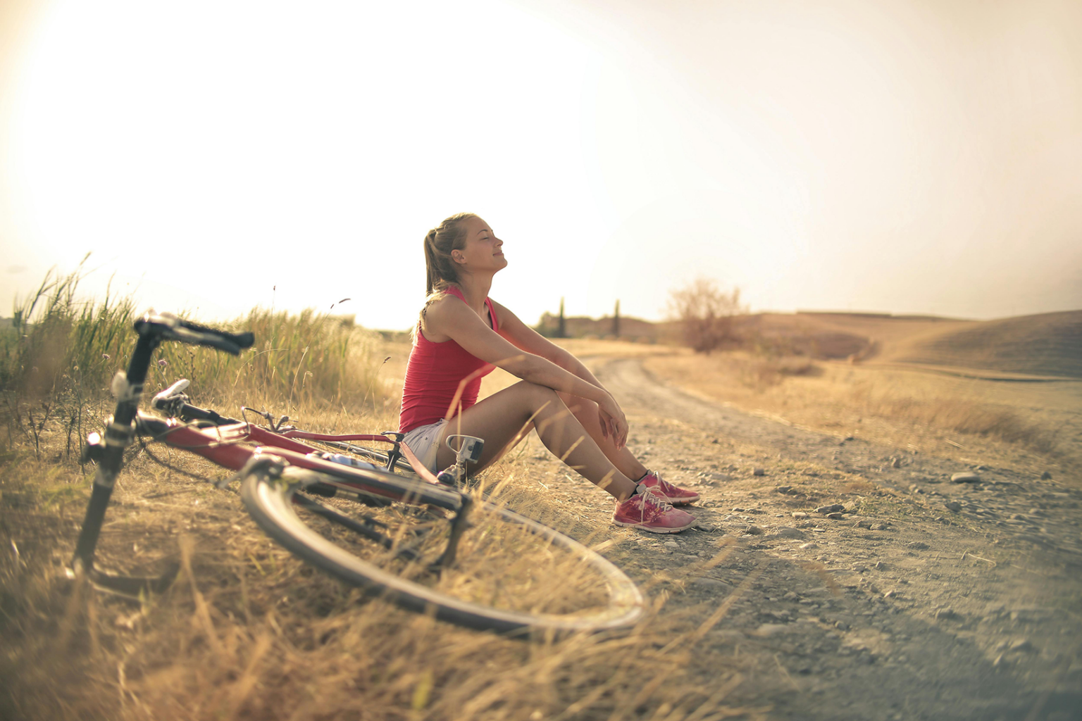 A woman sitting on a dirt road beside her bicycle.