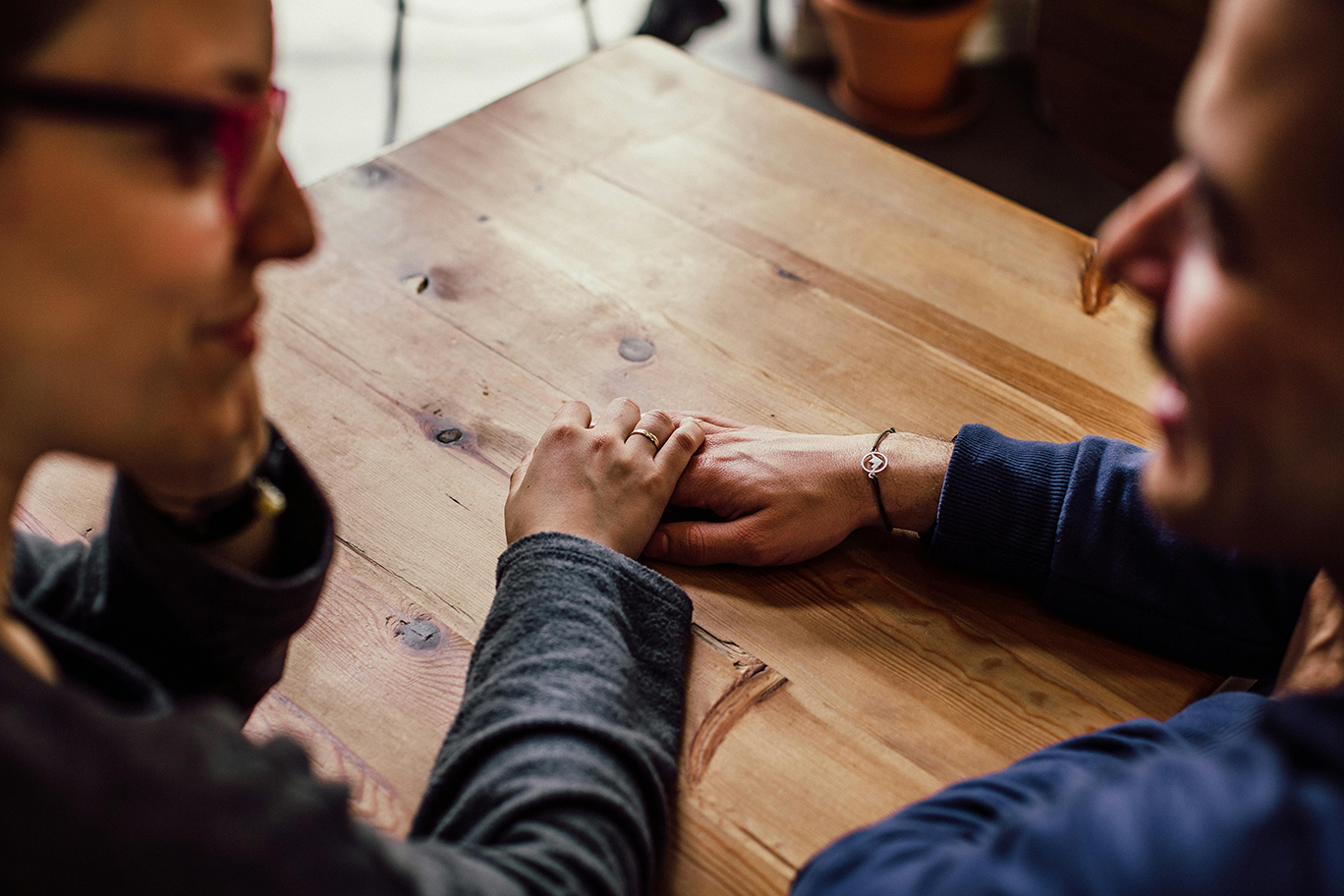A couple holding hands on top of a wood table.