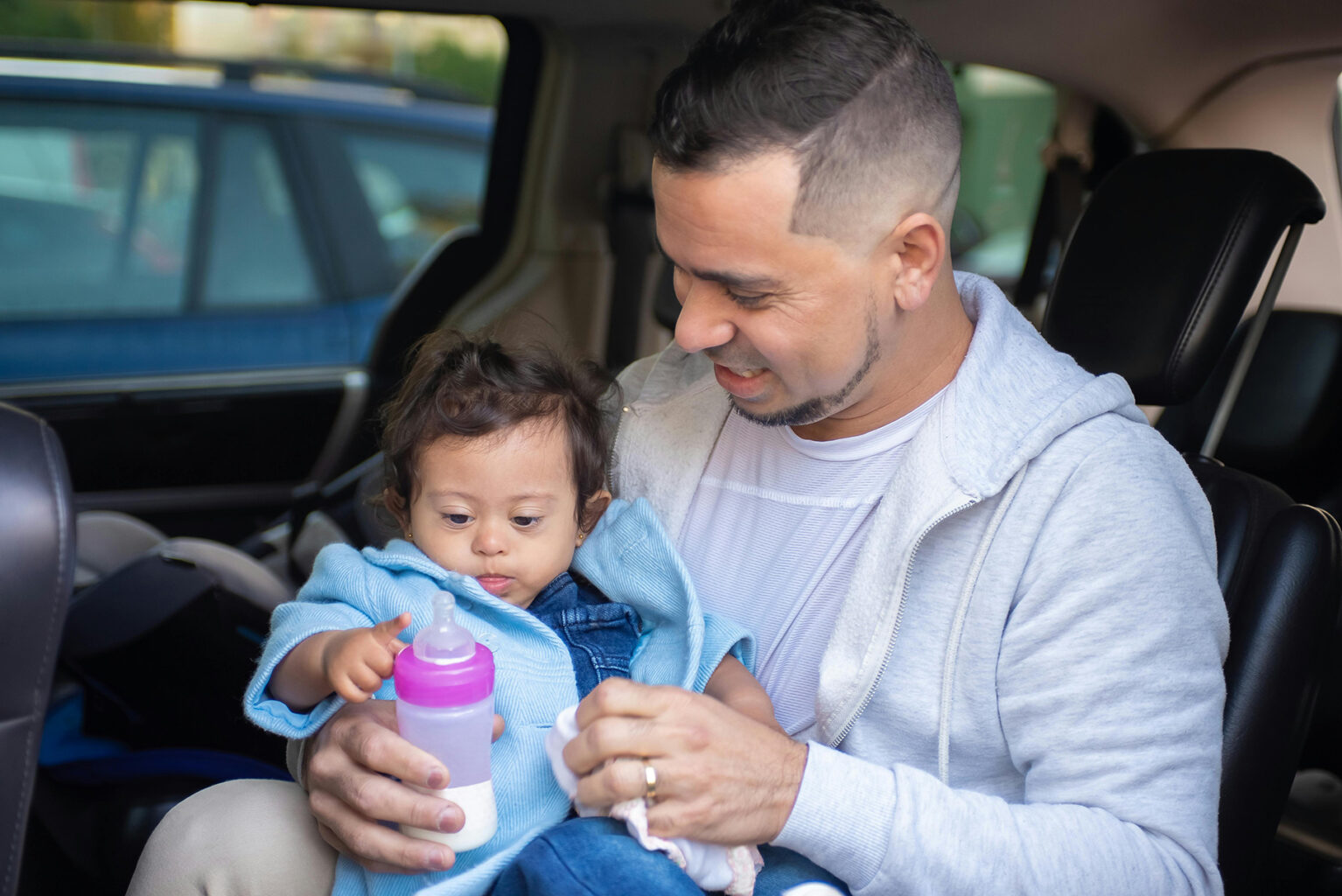 A dad feeding his baby a bottle of milk in a car.