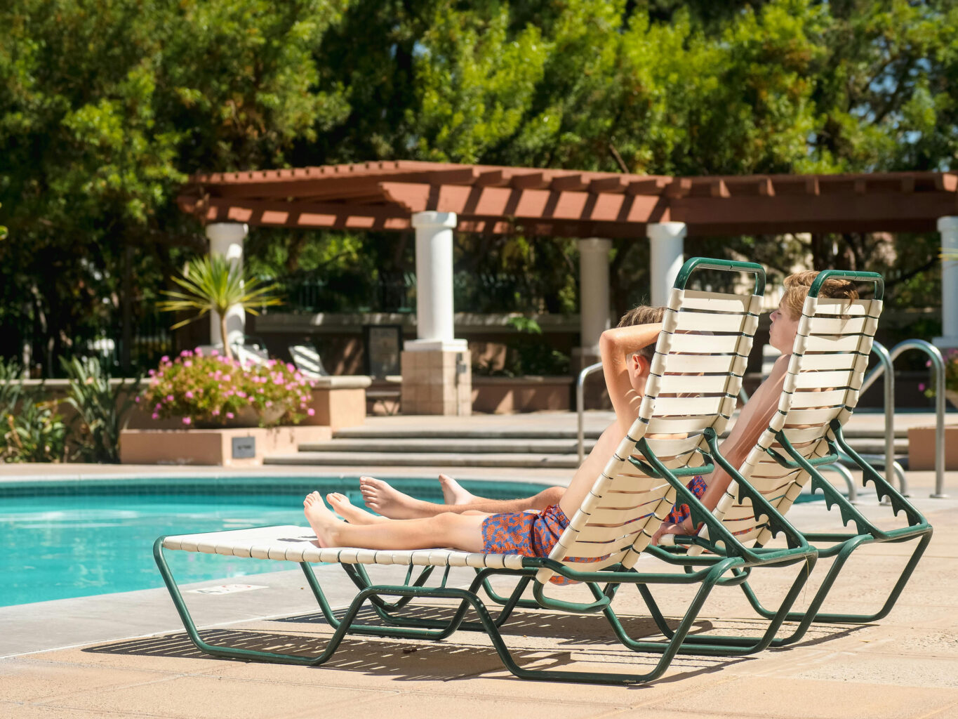 Two boys sitting in lounge chairs by a pool during summer break.