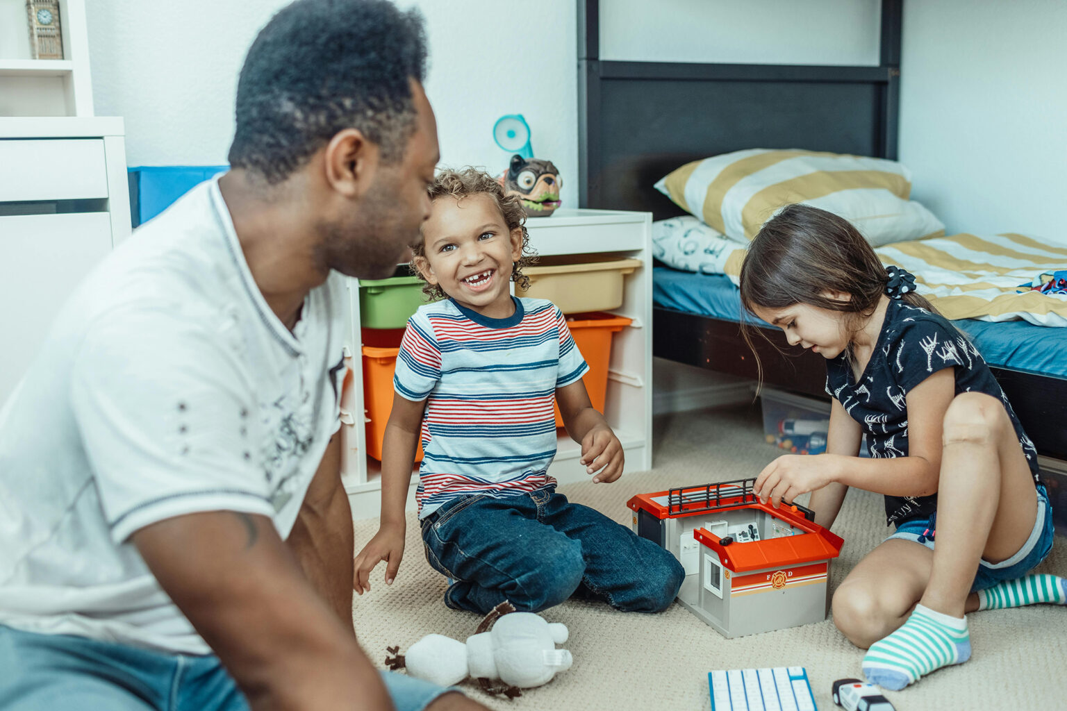 A father, son, and daughter playing a storytelling game on the floor with toys.
