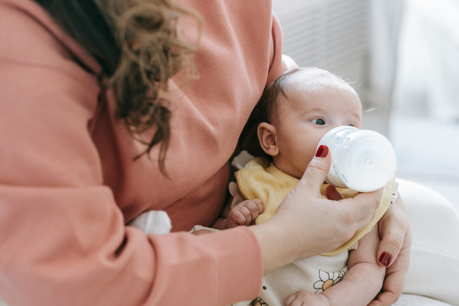A mother feeding her baby a bottle of breast milk on a couch.