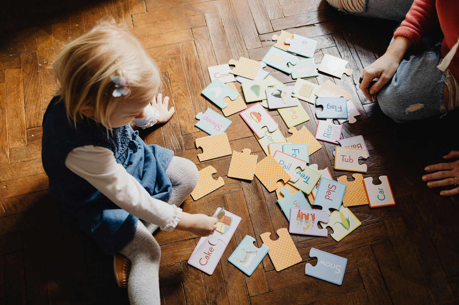 A child playing a language card game while sitting on a wood floor.