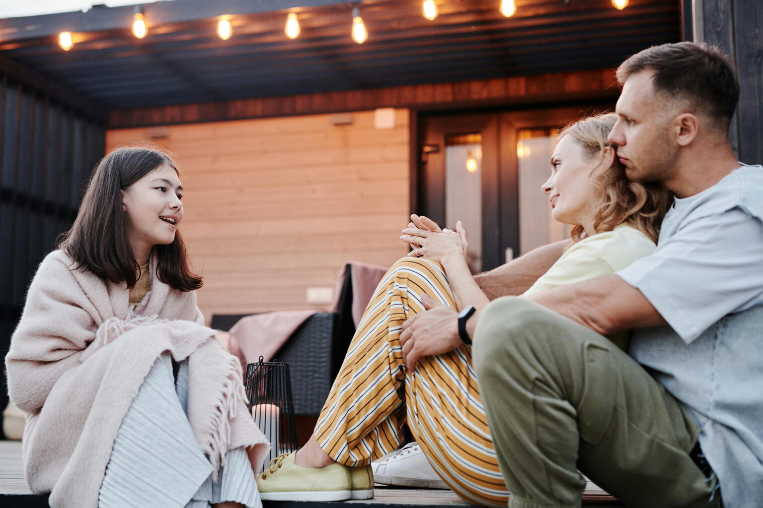 Daughter having a conversation with her parents while sitting outside on a back porch.