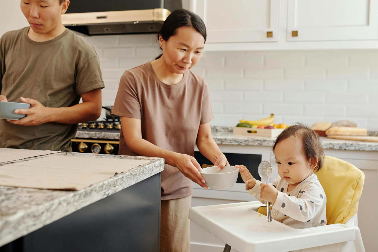 A mother bringing a bowl of baby food to her baby sitting in a high chair.