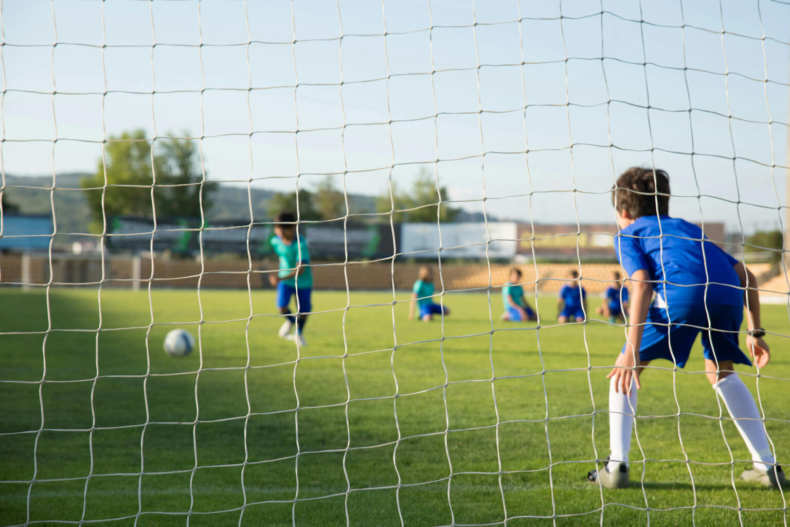 Kids playing soccer as seen through the soccer goal net.