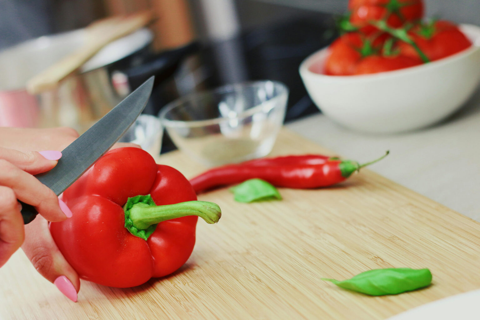 Woman slicing a pepper on a wooden cutting board.