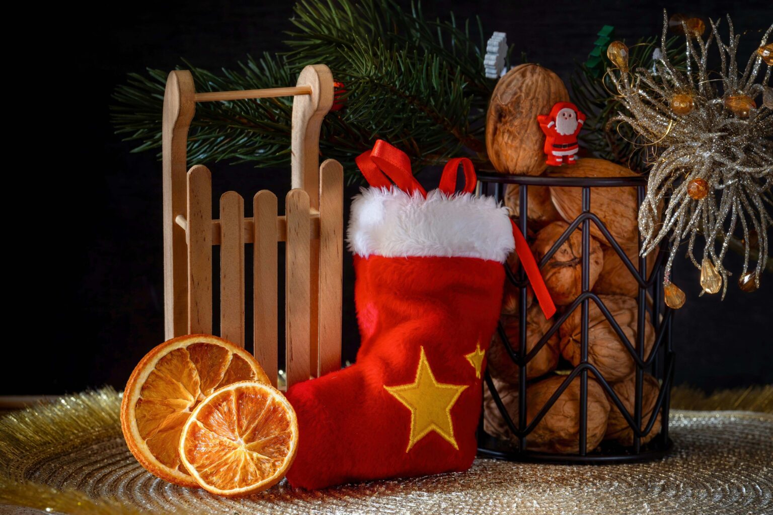 A christmas stocking next to walnuts, a miniature wooden sled, orange slices, and fir tree brances