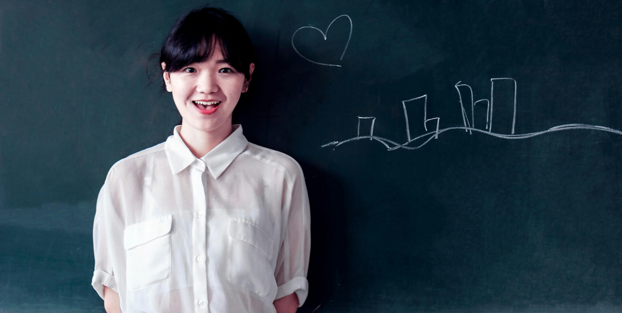A teacher standing in front of a chalk board with a hand-drawn heart and city skyline.