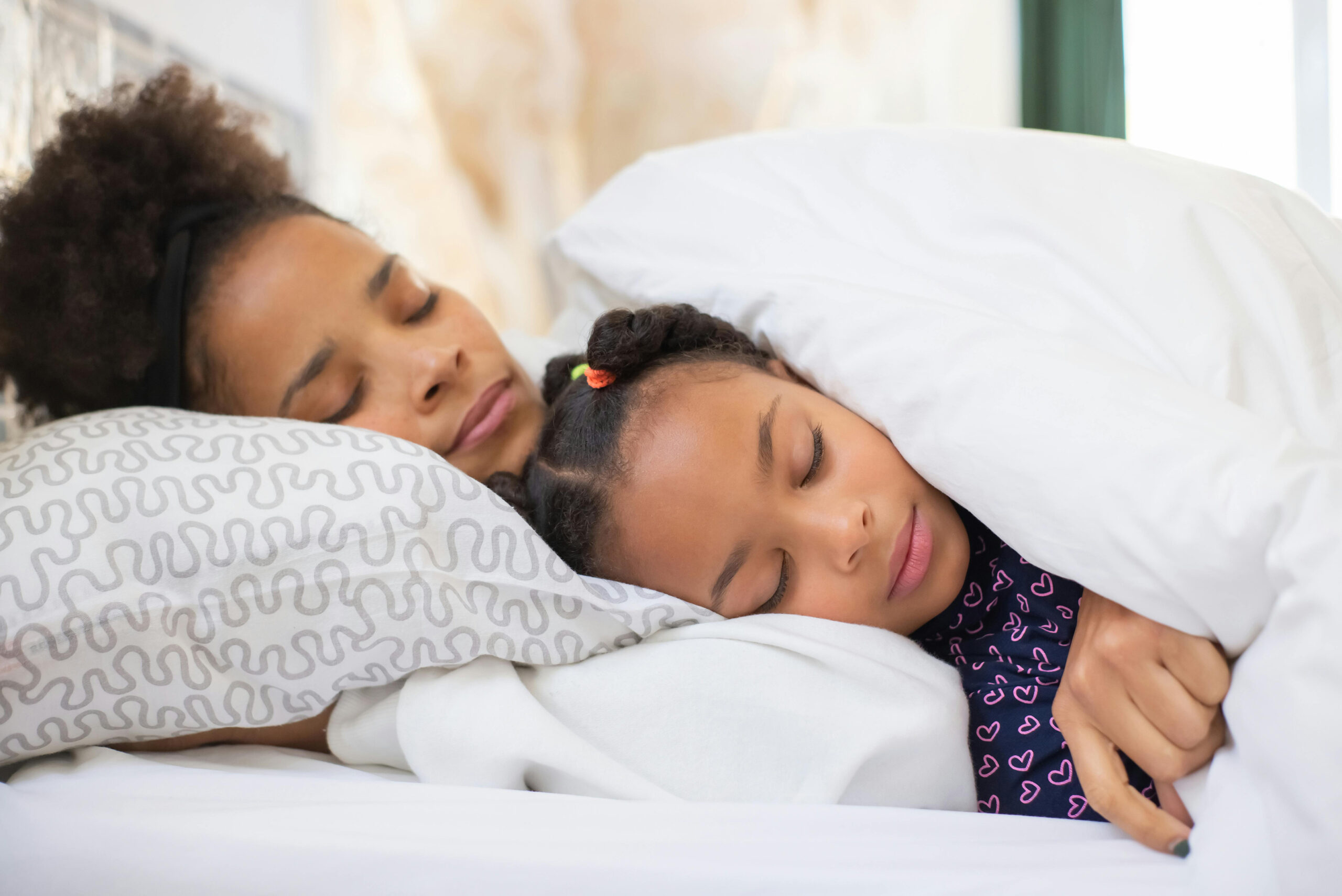 A mom and child sleeping on a bed.