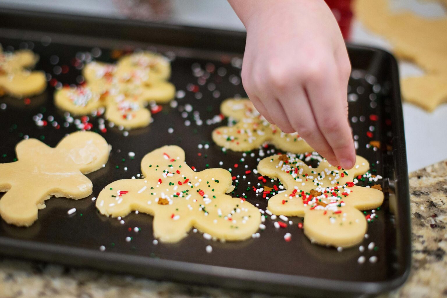 A child adding sprinkles to gingerbread cookies on a cookie tray.