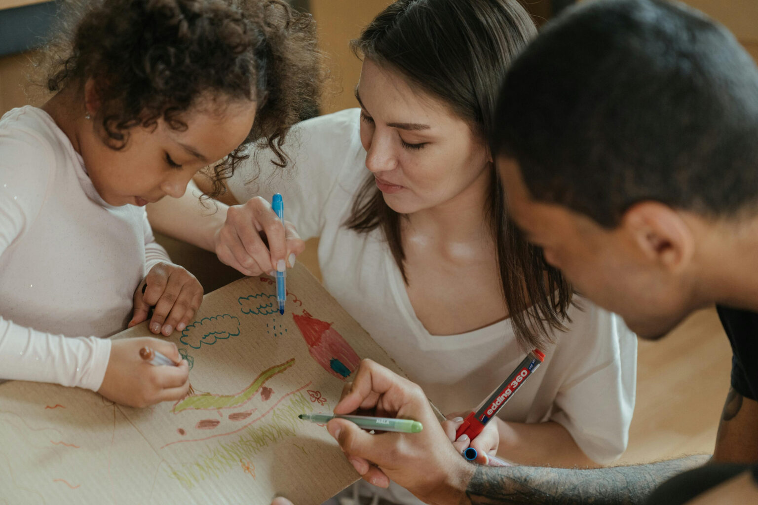 A mother, father, and daughter drawing on a paper.