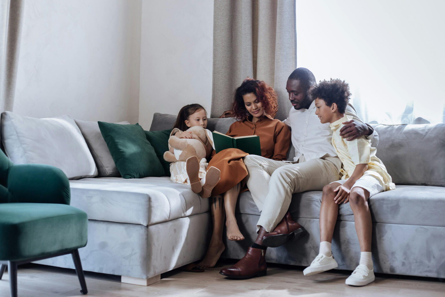 A father, mother, and two kids reading a book on a couch.
