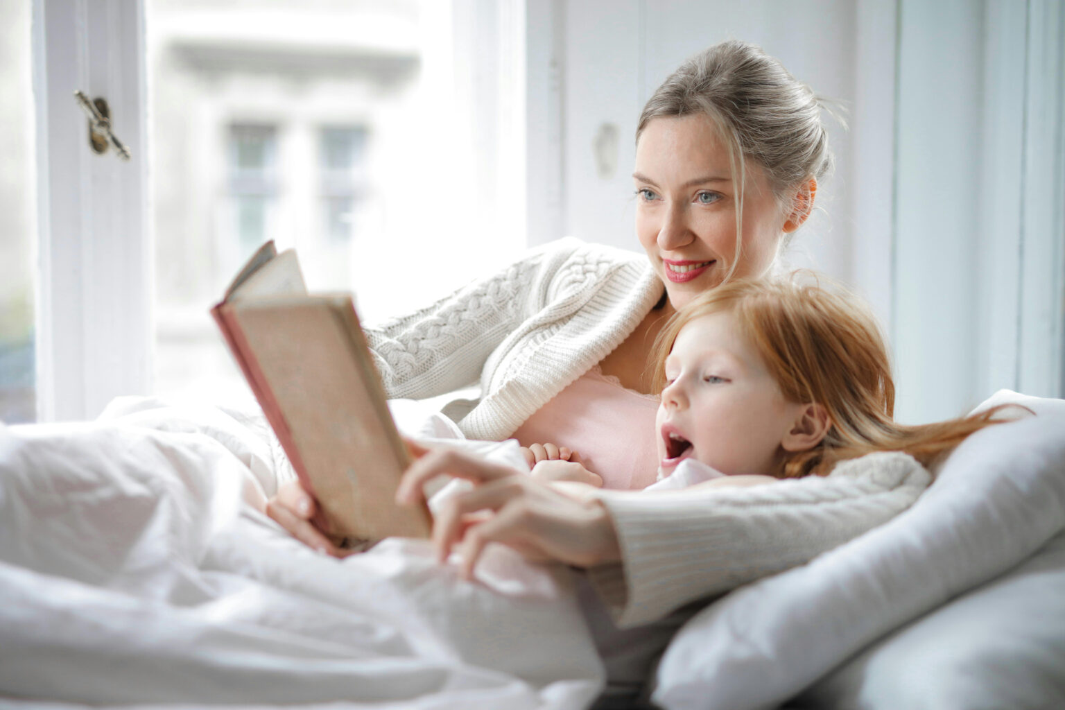 A mother and daughter reading a book together while lying on a bed.