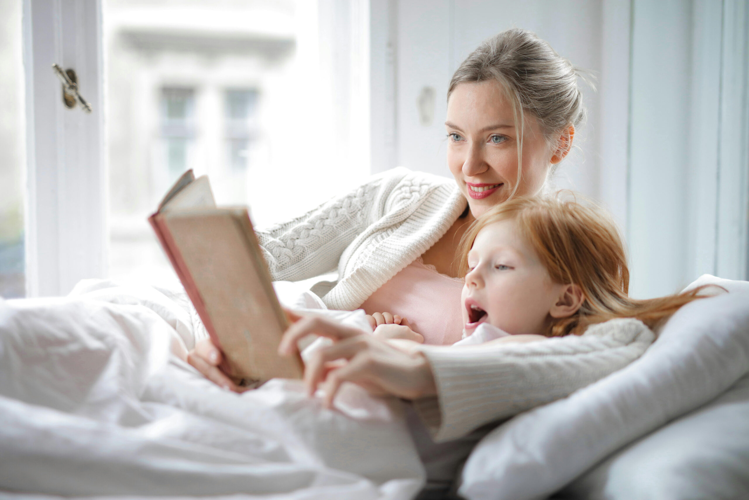 A mother and daughter reading a book together while lying on a bed.