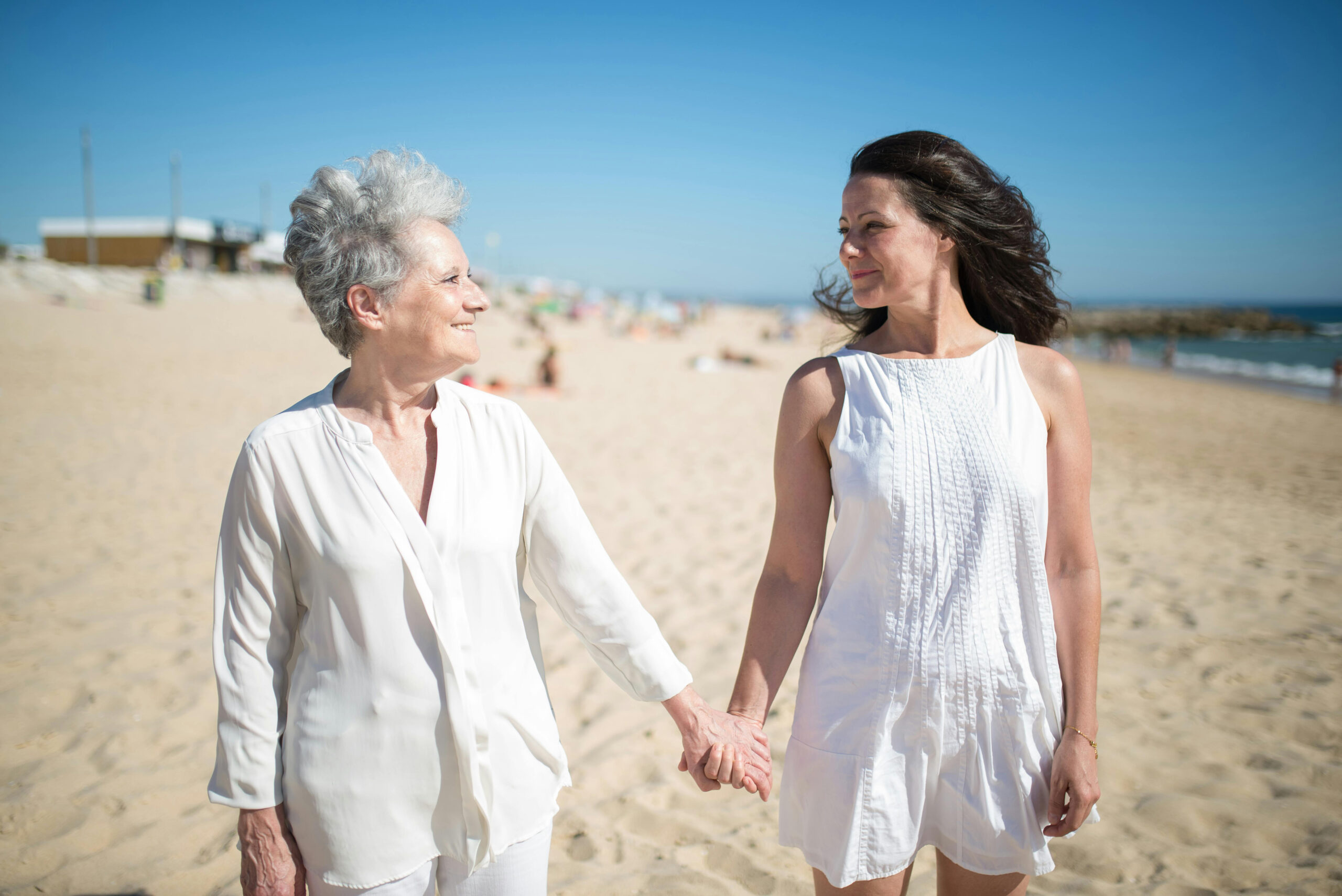 A mother and daughter walking along a beach holding hands.