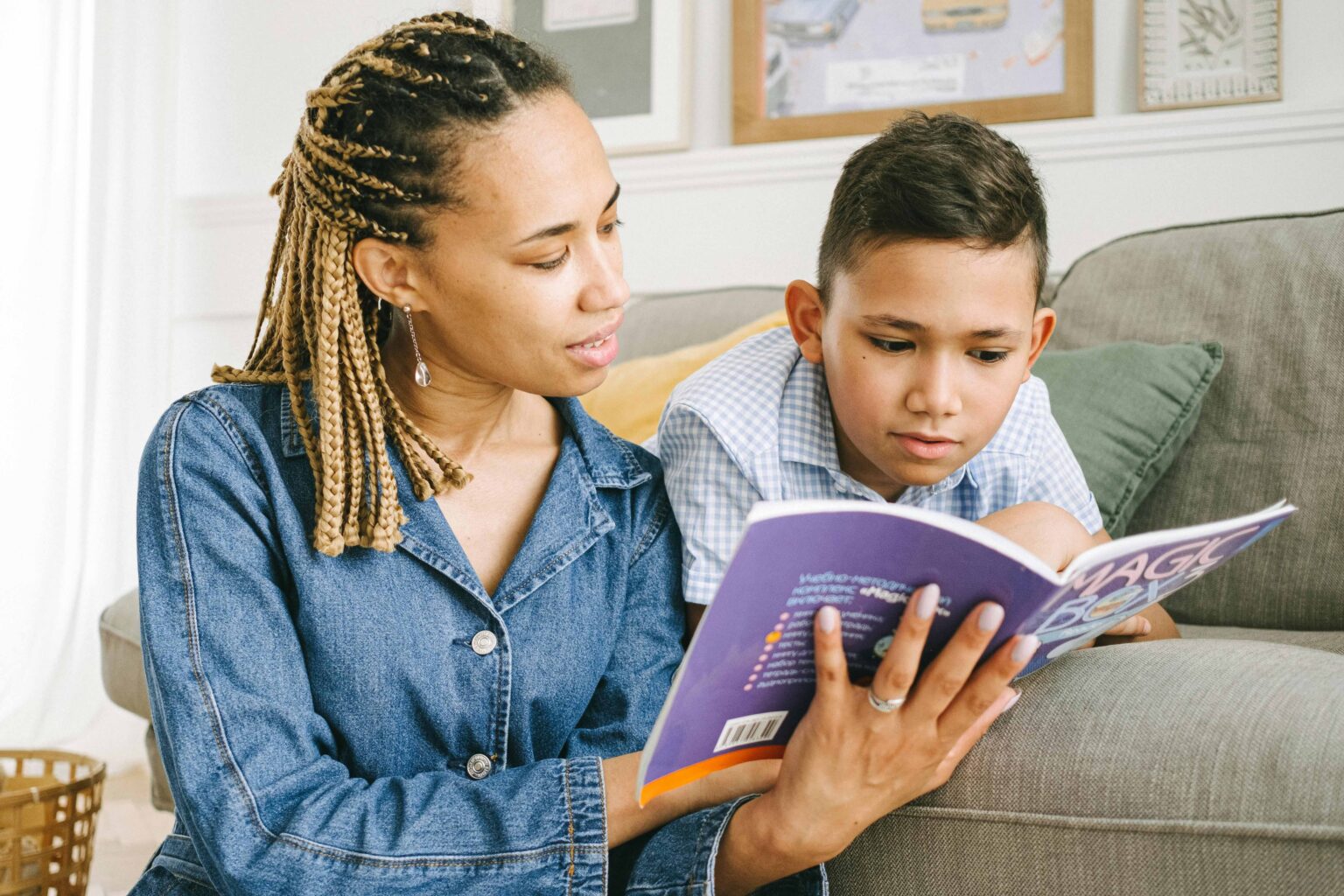 Mother and son reading a book together while mother sits on the floor and son sits on the couch.
