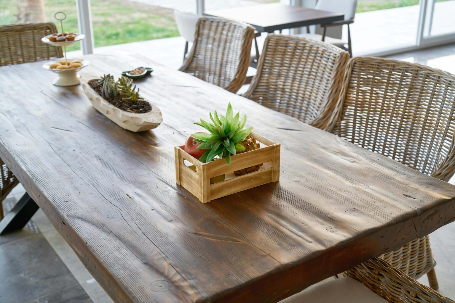 A wood table with two plants on top and three wicker chairs