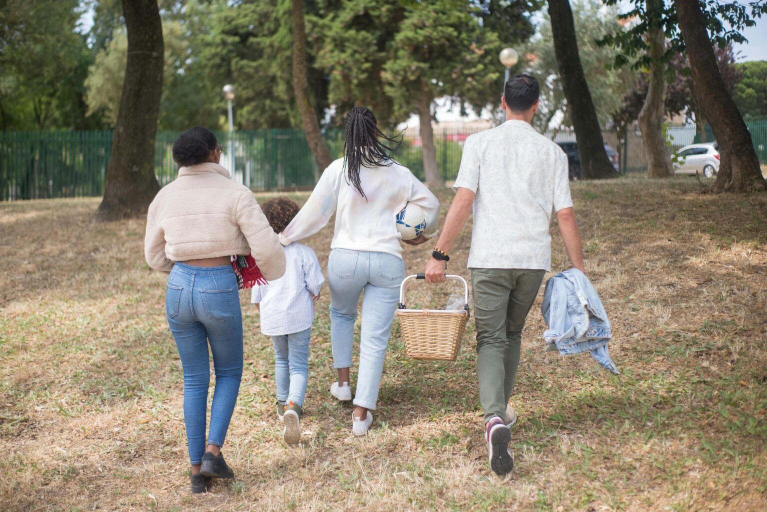 A family of four walking in a park with a picnic basket and blanket