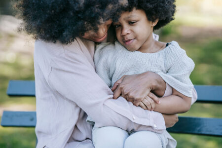 A mother hugging daughter on a bench outside