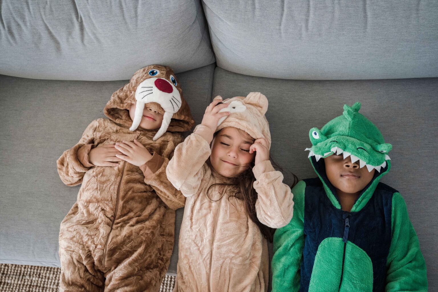 three kids wearing costumes while lying on a couch